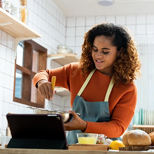 Young African American woman live streaming online with tablet computer while cooking 