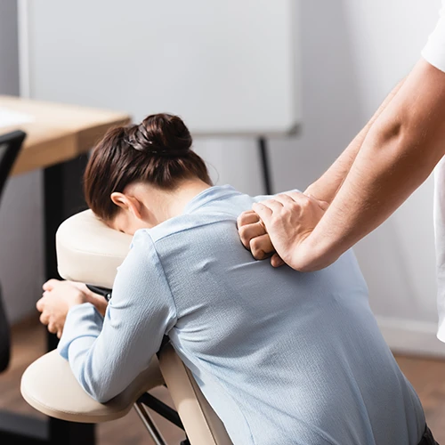 Massage therapist massaging brunette woman back sitting on massage chair